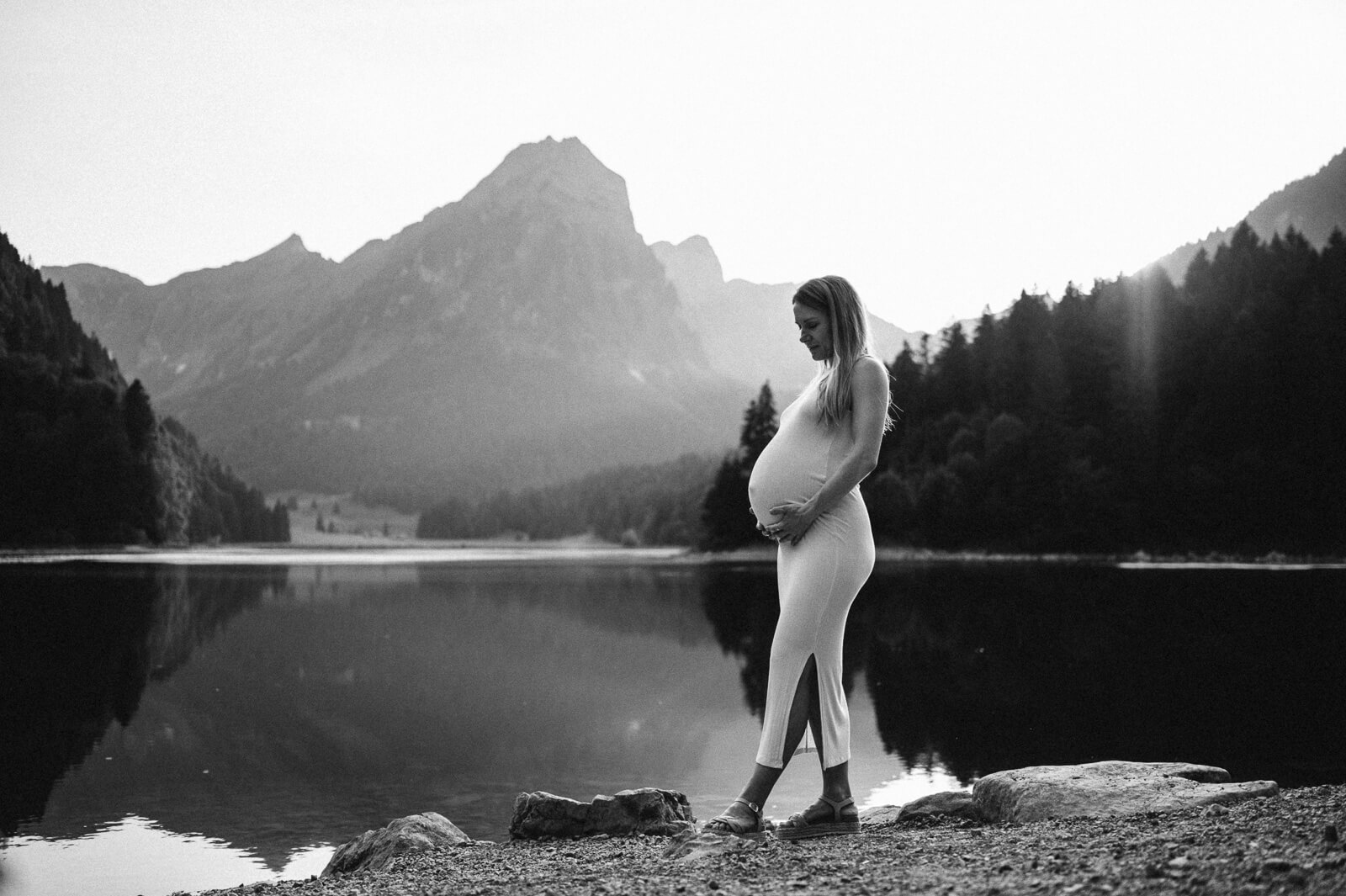 Schwarzweissbild einer schwangeren Frau an einem Bergsee in der Schweiz von einer Schwangerschaftsfotografin aus Zürich